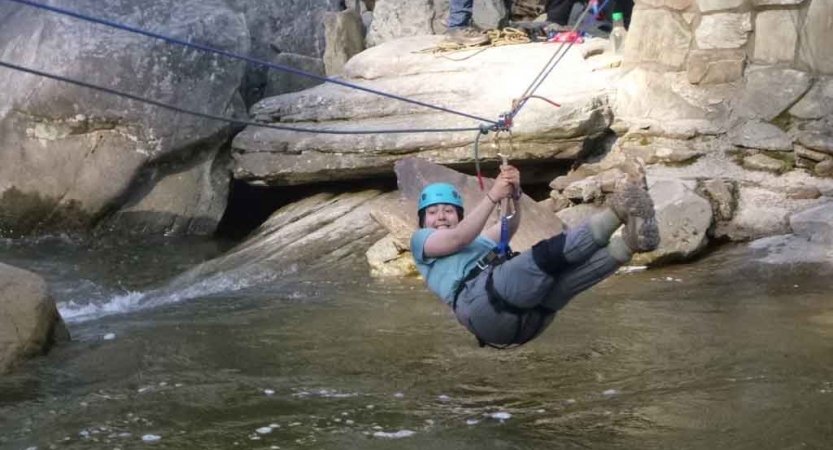 A person wearing safety gear crosses a river via the Tyrolean traverse